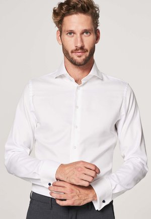 White dress shirt, long sleeves, front buttons, contrasting dark button accents on cuffs, smooth fabric, fitted design.