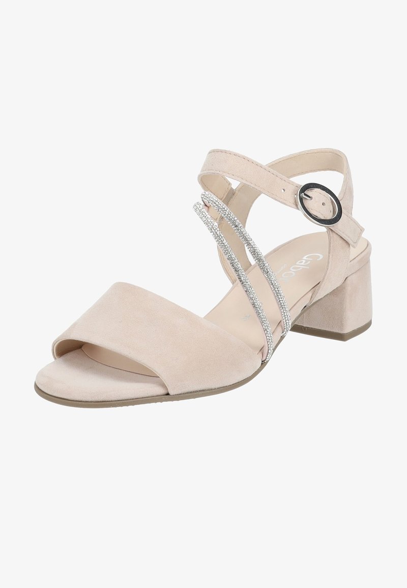 Sandale en suède beige clair dotée d'une large bride au niveau des orteils, d'une bride à la cheville avec boucle, et de deux lanières métalliques brillantes traversant le pied. Talon bloc bas.