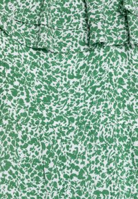 Zielono-biała tkanina w kwiatowy wzór o teksturowanej powierzchni. Posiada falbanę na górze i zakładki poniżej.