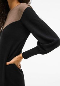Abito pull-over con un corpo nero e pannello spalle marrone. Presenta maniche lunghe e gonfiate con polsini a costine, realizzato in tessuto morbido.
