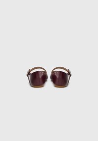 Chaussures en cuir marron foncé avec un bout rond et une bride à l'arrière. Présentent une boucle et une texture lisse avec une semelle de couleur claire.