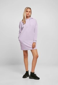 Rochie cu glugă lavandă, cu o croială relaxată, șnur ajustabil, mâneci lungi și buzunare. Pantofii sport negri completează ținuta.