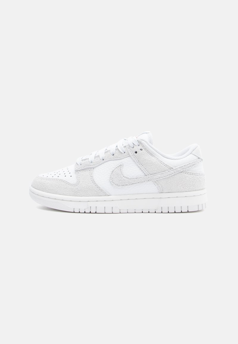 Baltie Nike kedas ar teksturētu ādu un zamšu, zemu augstumu, apaļu purngalu un rakstainu gumijas zoli.