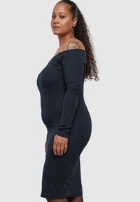 Svart ribbet kneleng dress med lange ermer og skulderavskåret hals, med en figurnær silhuett og glatt tekstur.