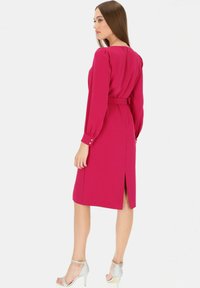 Sukienka do kolan, dopasowana, w intensywnym różowym kolorze; długie, bufiaste rękawy; talia podkreślona paskiem; rozcięcie z tyłu; w połączeniu z srebrnymi sandałami na wysokim obcasie.