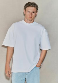 Camiseta blanca de algodón de gran tamaño con mangas cortas, escote redondo, combinada con unos vaqueros de denim azul claro. Textura suave y corte relajado.