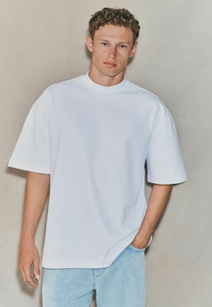 White oversized cotton t-shirt with short sleeves, round neckline, paired with light blue denim jeans. Smooth texture and relaxed fit.