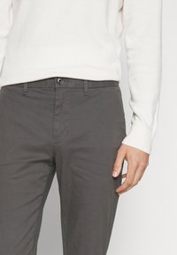 Szare bawełniane chinosy z zapięciem na guzik, bocznymi kieszeniami i gładką teksturą, połączone z białym swetrem.