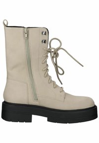 Beige veterschoenen tot de enkels met een gewatteerde tong, zijrits en stevige zwarte zool. Voorzien van een ronde neus en metalen veterogen.
