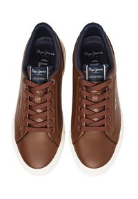 Zapatillas de cuero marrón con suela blanca, diseño con cordones, superficie texturizada y logo en la lengüeta. Interior forrado con material oscuro.