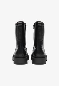 Botas de tornozelo em couro preto com um acabamento suave, fecho de zip na lateral e sola robusta. Detalhe de costura vertical na parte de trás.