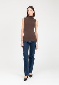 Top smanicato marrone con collo alto realizzato in tessuto a coste, abbinato a jeans dritti blu scuro e tacchi a punta neri.