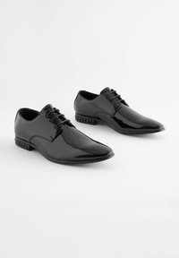 Chaussures de ville en cuir verni noir avec un bout pointu, un design à lacets et un accent texturé près du talon. Surface lisse et silhouette élégante.