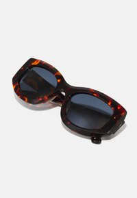 Óculos de sol estilo gato com armação de tartaruga escura, lentes escuras e forma angular. Apresenta hastes largas e acabamentos brilhantes.
