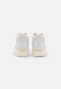 White sneakers with grey suede accents, textured back panel, and a cream rubber sole. Features a low-top design and lace-up closure.