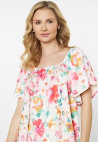 Blusa floreale con scollo quadrato e maniche a sbuffo corte. Realizzata in tessuto leggero con motivi floreali multicolori nei toni di rosa, verde e giallo.