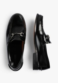 Mocasines de cuero negro con un acabado brillante, que cuentan con un detalle de hardware en tono plateado en la correa y un tacón de madera apilada.