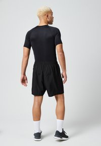 Zwarte sportoutfit bestaande uit een nauwsluitend shirt met korte mouwen en losse shorts, gemaakt van lichtgewicht, ademend materiaal.