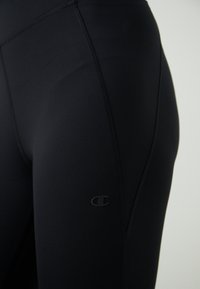 Fekete sportleggings nyújtható anyagból, szoros illeszkedéssel és látható varrás részletekkel, az oldalán egy kis fekete logóval.