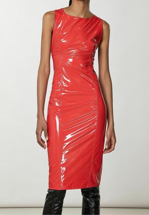 Sleeveless, shiny red midi dress with fitted silhouette worn with black shiny boots, shown from neck to mid-calf against plain background.