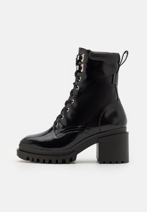 Bottine noire brillante en cuir à lacets jusqu'à la cheville avec un talon bloc épais et une semelle robuste, équipée d'œillets métalliques et d'une languette arrière.