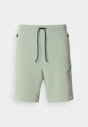 Mint green shorts made of soft fabric, featuring an elastic waistband with black drawstring and a side pocket displayed with a logo patch.