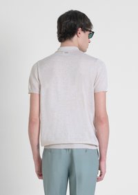 Polo shirt a maniche corte color beige chiaro con un fine punto a maglia. Colletto e polsini a coste, indossato con pantaloni turchesi.