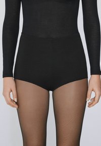 Hoge zwarte shorts van gladde stof, gecombineerd met doorschijnende zwarte panty’s. De outfit heeft een geribbeld lange mouwen top.