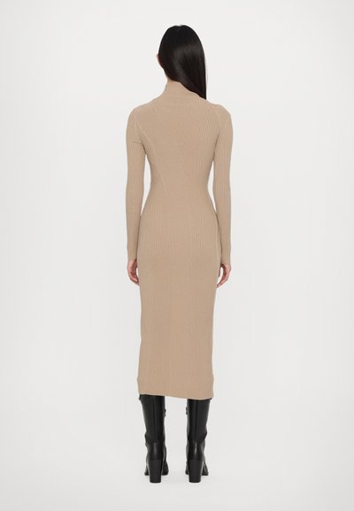 Beige ribbed midi dress with long sleeves and a high neck; form-fitting silhouette. Paired with black knee-high heeled boots.