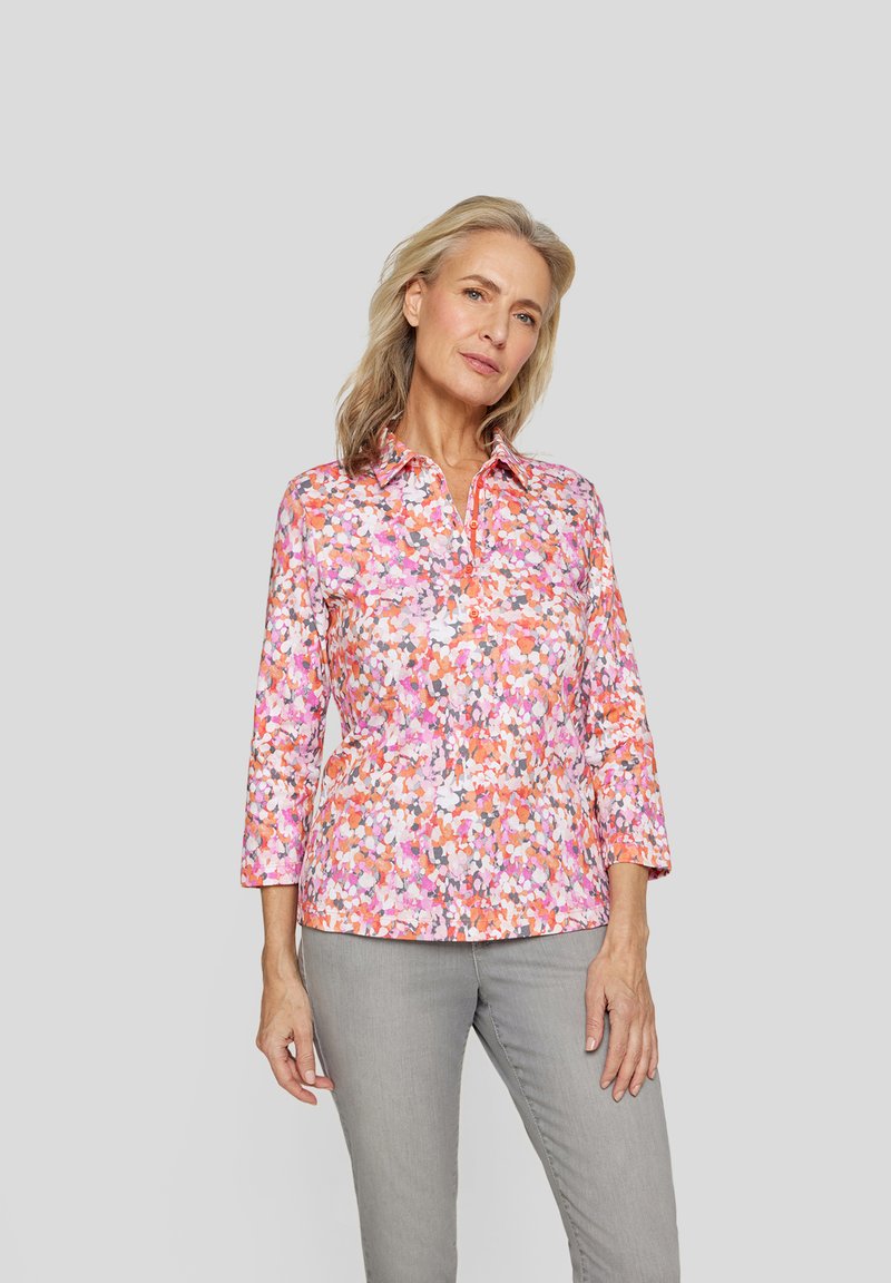 Bunte Blumenbluse mit einem Kragenhals, Dreiviertelärmeln und lockerer Passform. Enthält Farbnuancen von Pink, Orange und weißen Mustern.