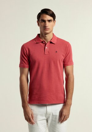 Camisa polo de algodón roja con cuello y mangas cortas, que presenta tres botones y un pequeño logo bordado en el lado izquierdo del pecho.