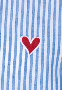 Sinine ja valge triibuline kangas, millel on brodeeritud punane südame motiiv. Muster koosneb erineva laiusega vertikaalsetest triipudest.