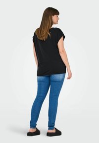 Haut noir à manches courtes, coupe ample, associé à un jean bleu skinny et des sandales noires. Tissu lisse, design sobre.