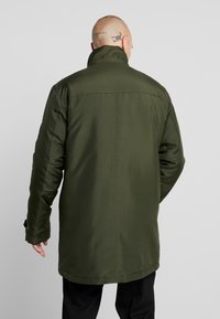 Zielona ocieplana kurtka z wysokim kołnierzem, długimi rękawami i prostym krojem. Charakteryzuje się gładką fakturą i subtelnymi detalami przeszyć.