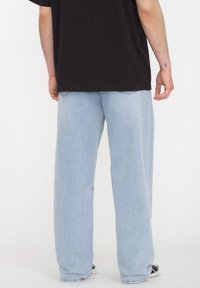 Jeans de denim de color azul claro, de corte holgado, que cuentan con un diseño clásico de cinco bolsillos y un corte recto. Detalles de costura simples visibles.