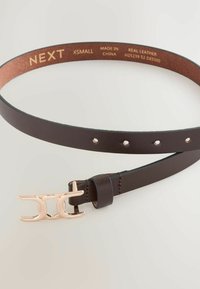 Hnědý kožený pásek s lesklou růžově zlatou sponou. Pásek má několik děr pro úpravu velikosti a hladký, elegantní povrch.
