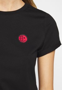 T-shirt noir avec un petit emblème rouge sur la poitrine montrant un design moitié globe et moitié visage souriant.