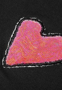 Czarny materiał z jasnoróżowym wzorem w kształcie serca, wyróżniającym się teksturą plastra miodu, obramowany czarnym przeszyciem. Brzegi wydają się postrzępione.
