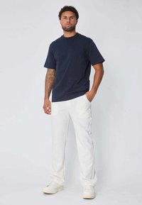 T-shirt bleu marine à col rond associé à un pantalon blanc. Le t-shirt a des manches courtes ; le pantalon est doté de poches et d'une coupe droite.