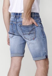 Pantalones cortos de mezclilla en azul claro con dobladillo vuelto, que cuentan con cinco bolsillos, costuras en contraste y una etiqueta de cuero en la cintura.
