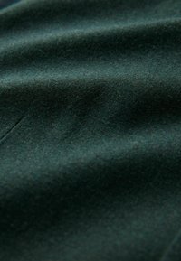 Tamsiai žalia medžiaga su minkštu, tekstūruotu paviršiumi, turinti švelnių raukšlių ir lygia išvaizda, greičiausiai pagaminta iš vilnos ar pana�šaus audinio.