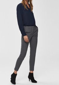 Mörkblå blus med V-ringning, grå skräddarsydda byxor och svarta ankelboots. Slät tygkvalitet med en figurnära design och avsmalnande byxor.