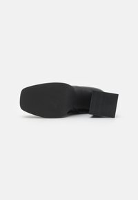 Zapato negro con punta redondeada, material superior liso, suela de goma texturizada y tacón grueso.