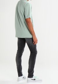 Zelené tričko s krátkým rukávem, měkká tkanina, volný střih. Doplněno o slim-fit tmavé džíny a bílé tenisky s černými akcenty.