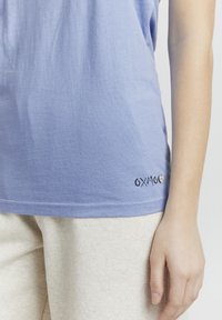Világoskék pamut póló rövid ujjakkal, az alsó bal szegélyen hímzett "OXMO" logóval. Puha, textúrált anyag.