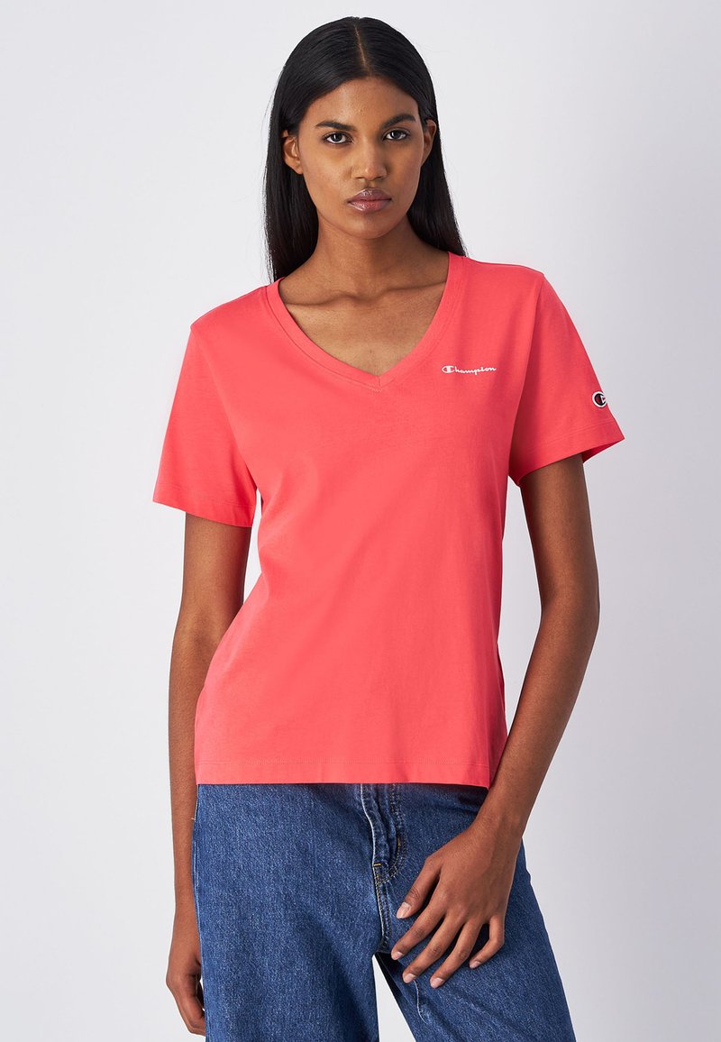 T-shirt corallo a V in cotone leggero con maniche corte; presenta un piccolo logo bianco sul petto e un logo sulla manica.