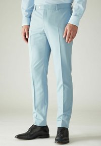 Lichtblauwe broeken met een maatwerk pasvorm, voorzien van een platte voorkant en zijzakken. Gecombineerd met zwarte leren nette schoenen.