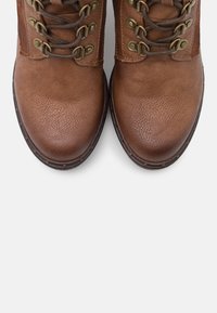 Bruine leren laarzen met een gestructureerde afwerking, voorzien van metalen oogjes en veters, een ronde neus en stevige rubberen zolen.