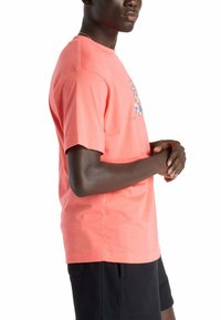 Camiseta de algodón en color coral con un estampado gráfico en la parte frontal, cuello redondo y mangas cortas, combinada con pantalones cortos negros.