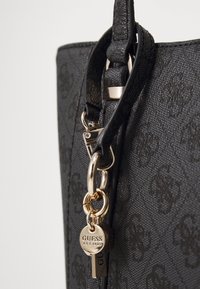 Musta tekstuurilla varustettu käsilaukku, jossa on kultaiset yksityiskohdat, avaimenperäkoristeita ja kiiltävä avainriipus, joka korostaa brändilogoa.